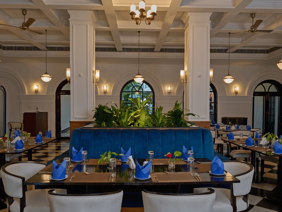 Elegant dining room at the best hotel in Fort Kochi, Old Court House by Abad, featuring a blue velvet booth, white columns, and set tables.