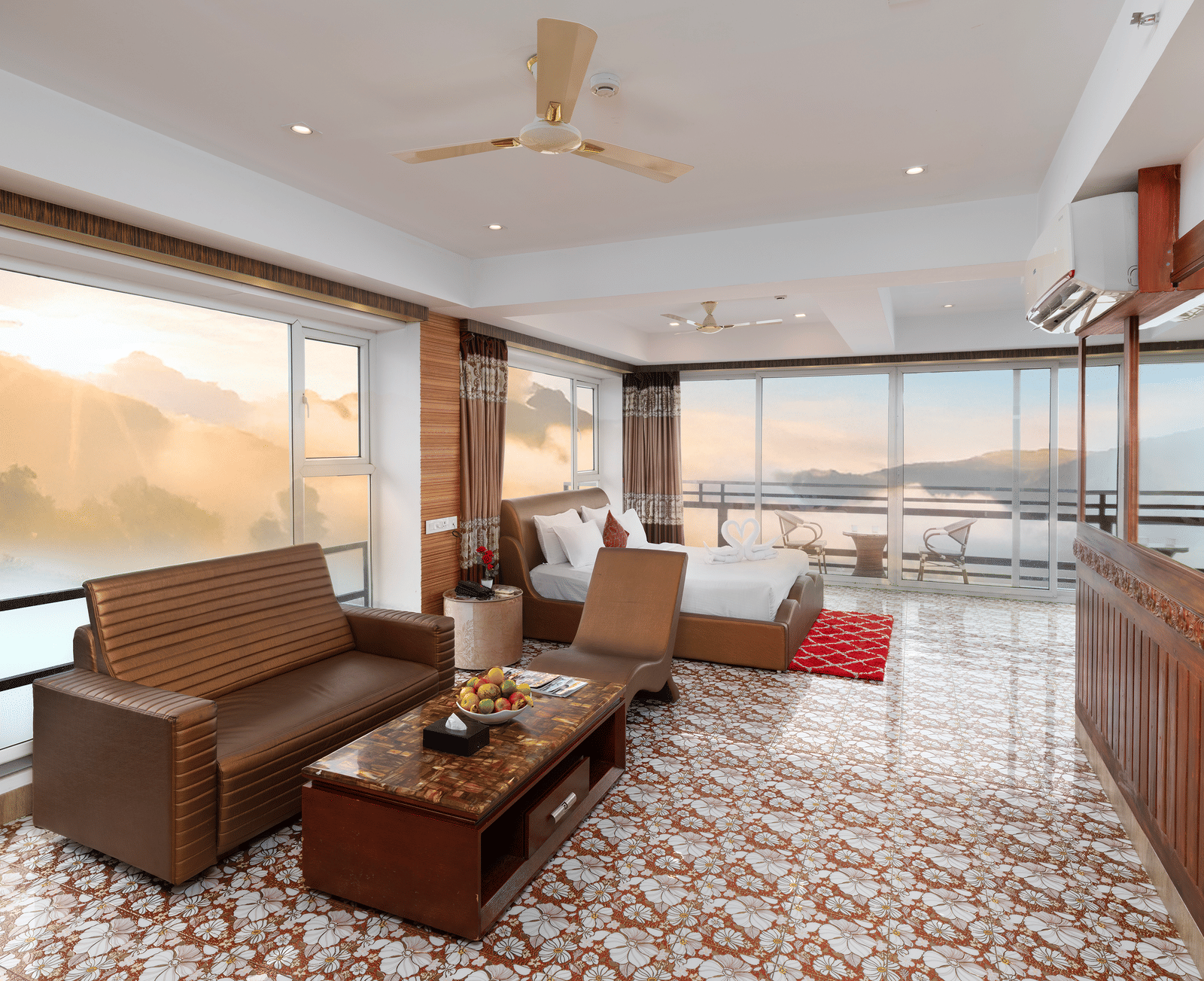 A spacious living area of the 180-Degree Club Suite at Parakkat Nature Hotel and Resorts, Munnar, featuring a multi-seating sofa, long wooden table, patterned carpet, and expansive windows with a wide, scenic view.