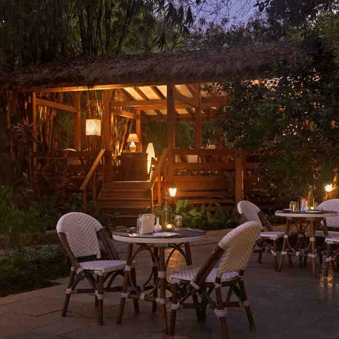 Outdoor dining area with elegant chairs and warm lighting in a garden at Amanvana Spa Resort, Coorg.