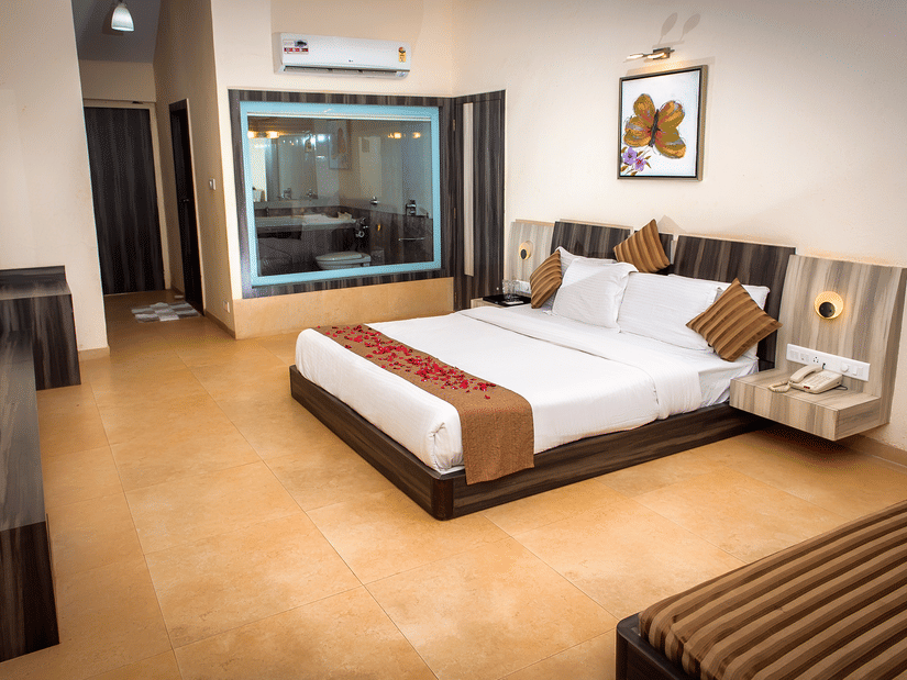 A view of the bed in Regency Room with its two side tables, glass window to the bathroom, diwan, and a consoel.