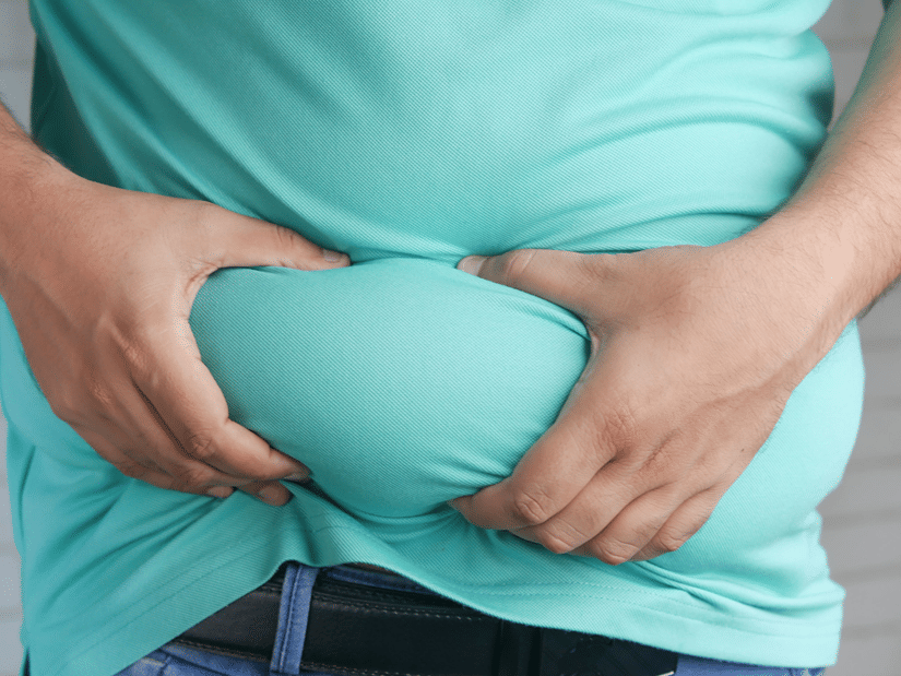 A man in a teal T-shirt pinching the fat around his belly with both hands