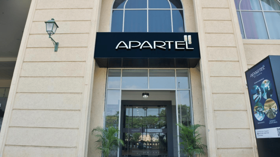 A close-up of a classical stone building facade featuring an arched entrance, a black sign, and a traditional green wall lantern at Apartel by Aarin, Oragadam.