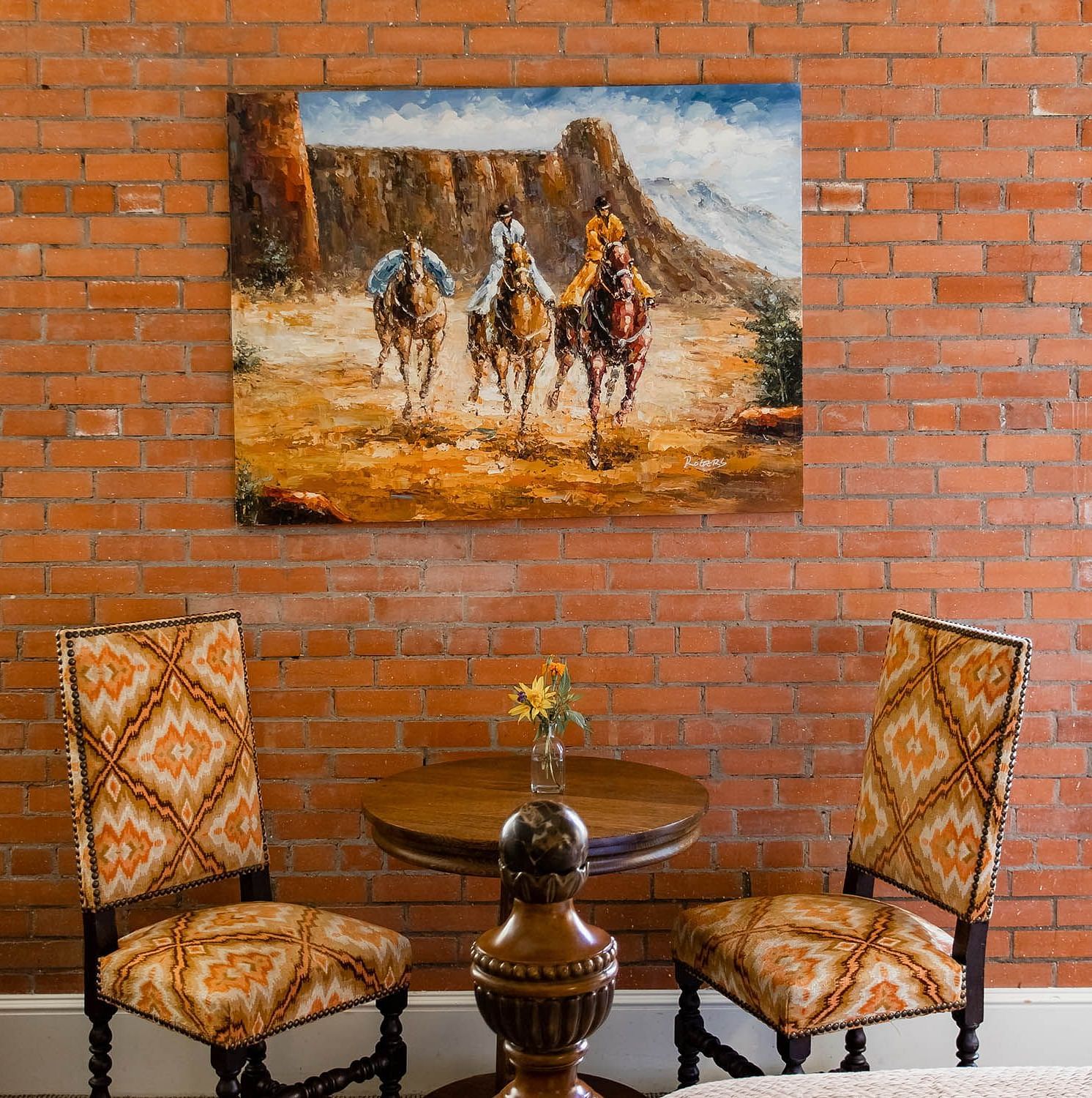 A room with a rustic brick wall, a beautiful painting of horses, and stylish seating, creating a warm, artistic atmosphere - The Grand Hotel & Ballroom, McKinney