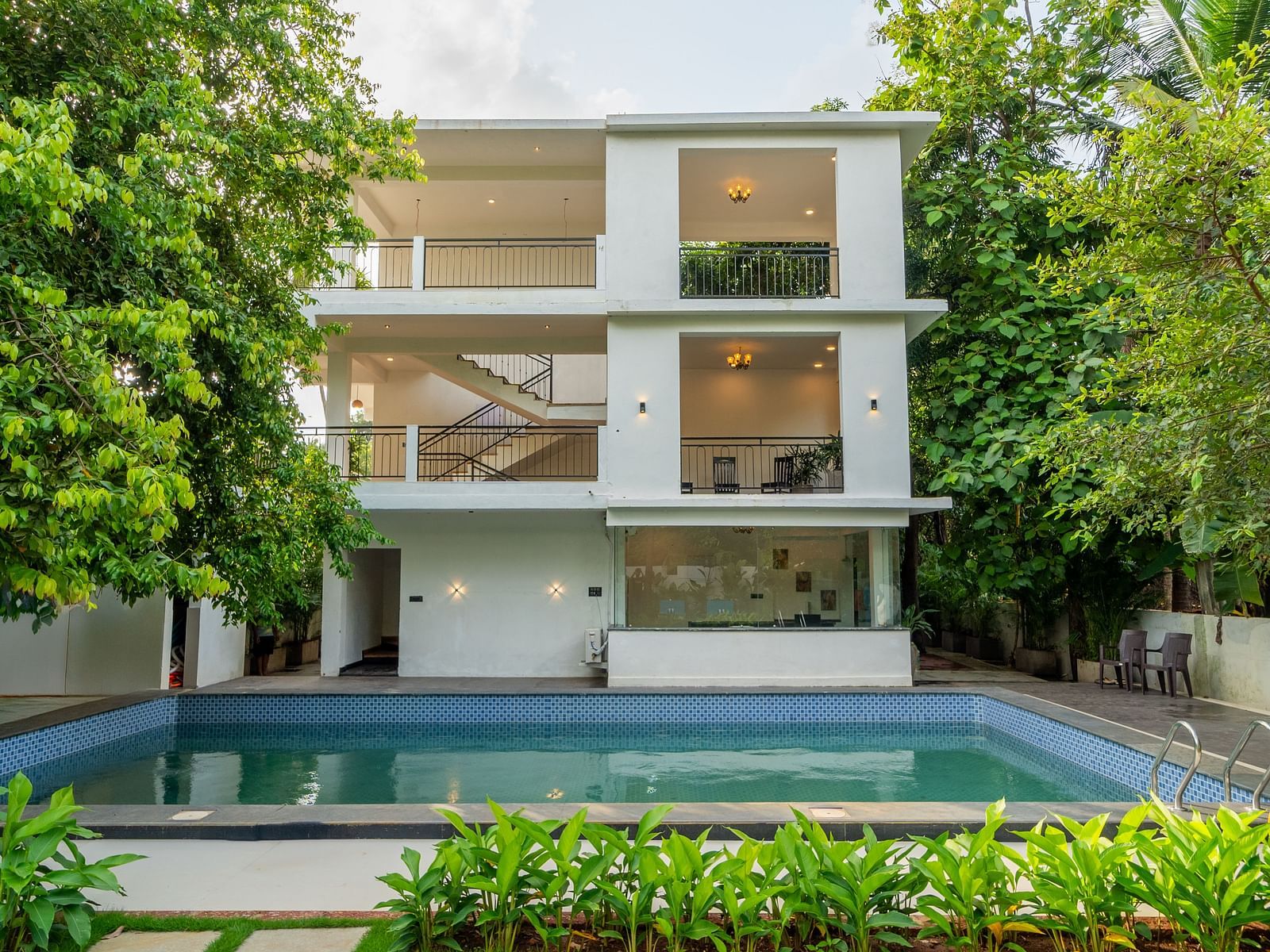 Modern white building with a swimming pool surrounded by greenery at De Soul Santé Hotels & Resorts.