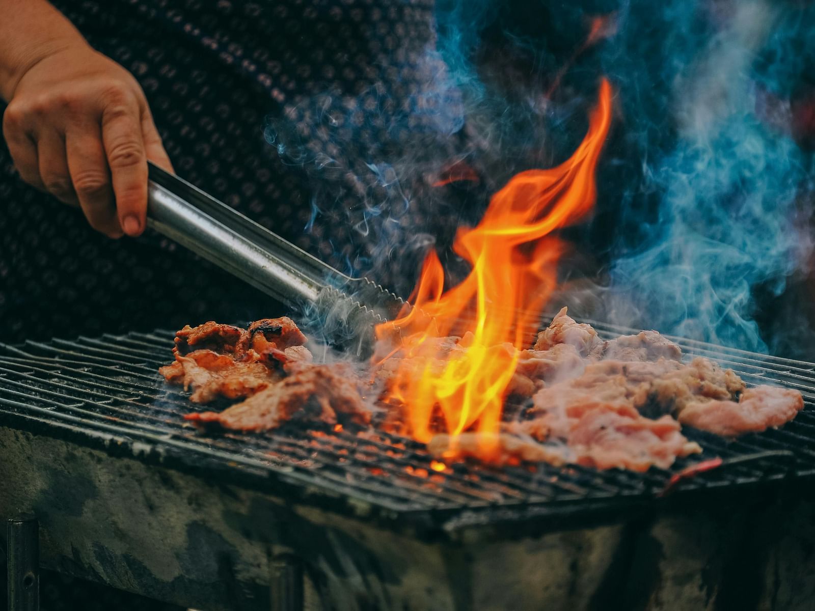 A hand grilling barbecue on a grill, with flames rising high, creating a lively and mouth-watering cooking scene