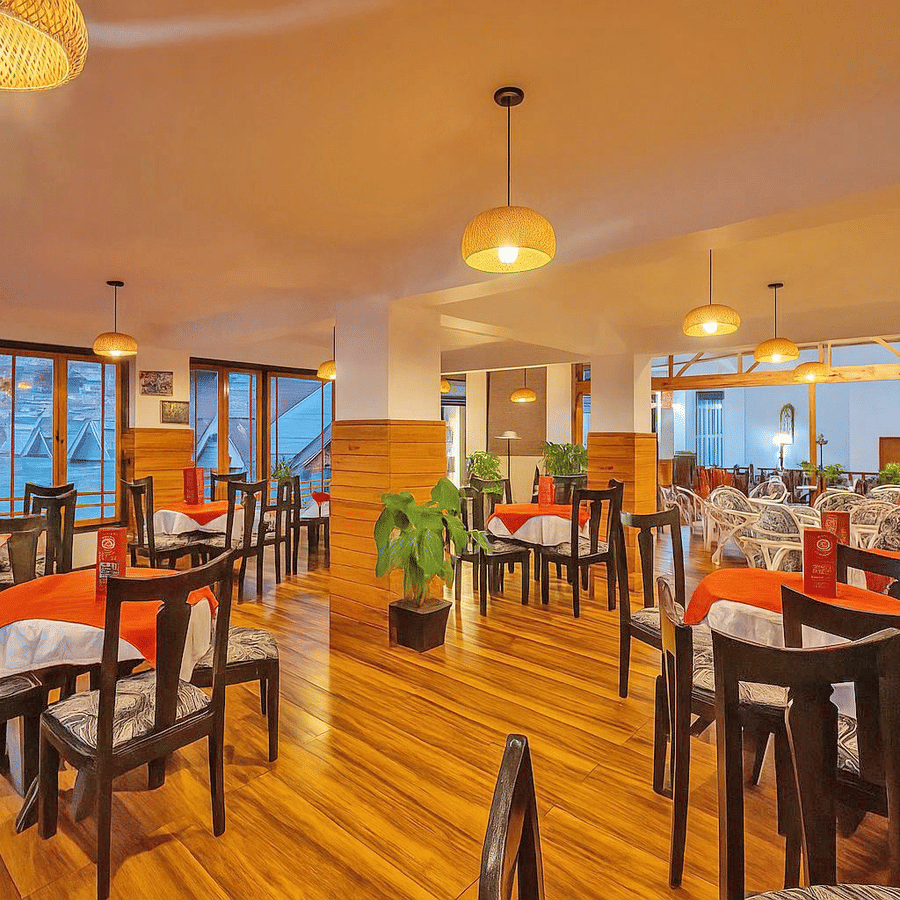 Orchid Restaurant at Central Heritage Resort and Spa, Darjeeling featuring ceiling lights, dining tables and chairs, and plants across the space.