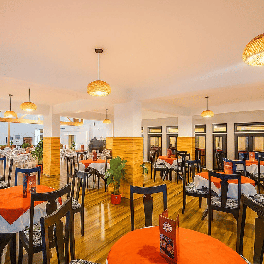 Orchid Restaurant at Central Heritage Resort and Spa, Darjeeling featuring several sets of dining table and chairs, and a ceiling light hanging from above