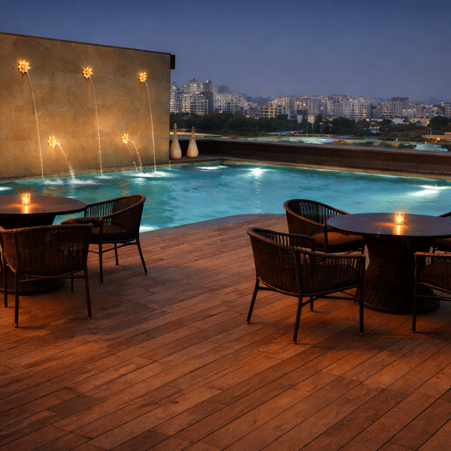 Illuminated rooftop pool deck at dusk featuring outdoor dining tables and chairs on wooden flooring.