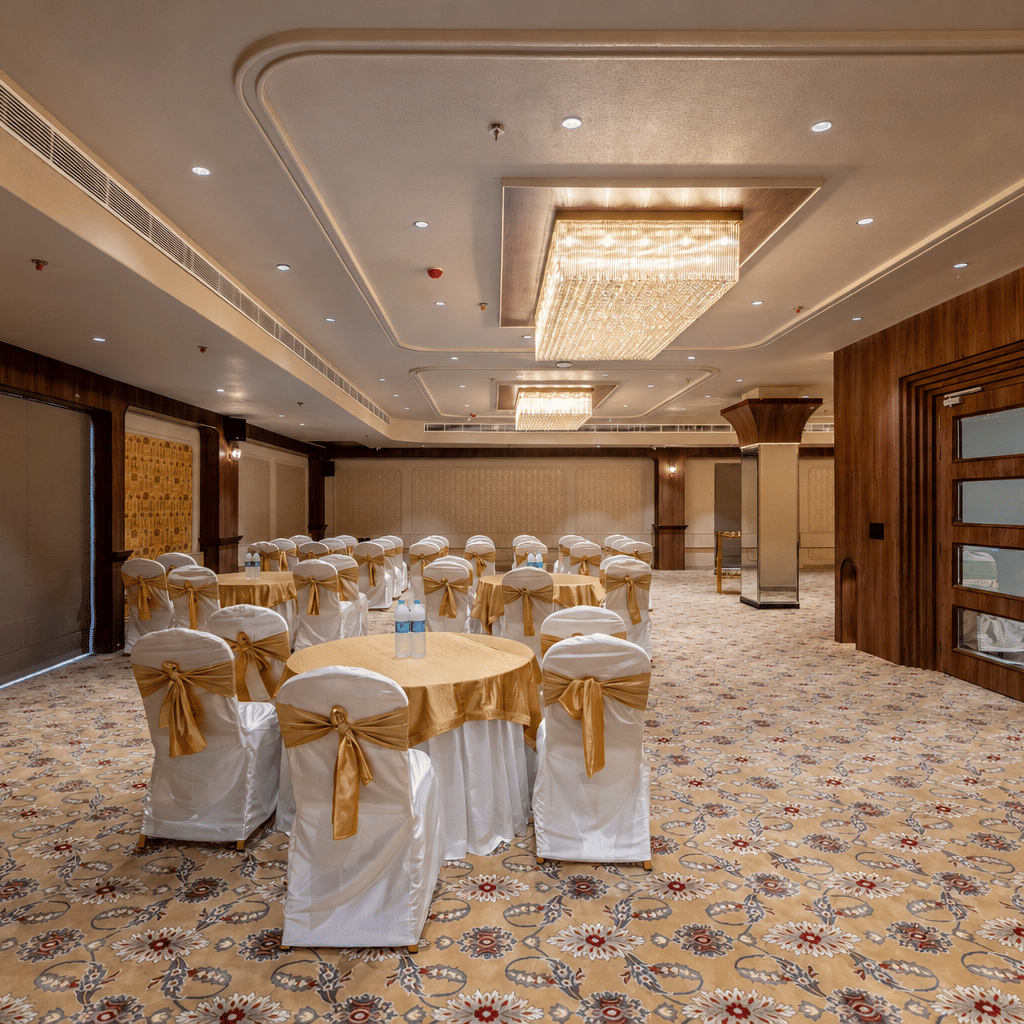 Banquet hall arranged with round tables, covered chairs, and decorative lighting.