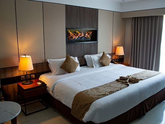 A room with a king bed, soft lighting, neutral tones, and a stylish wall-mounted artwork above the headboard.