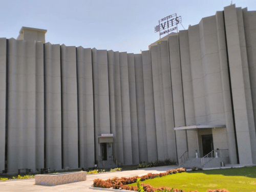 Facade of VITS Hotel in Jamnagar, Mithoi, on a sunny day featuring a multi-storey building surrounded by lawn under a clear sky
