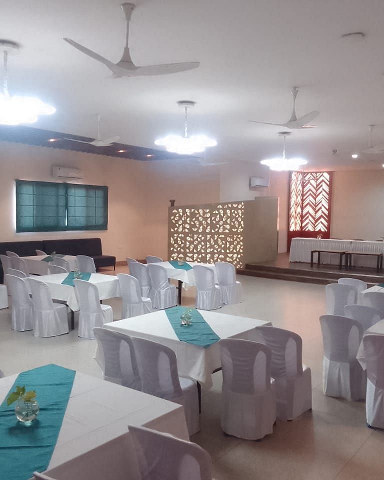 An event room with tables and chairs, a ceiling fan, and patterned curtains - Lords Eco Inn Belagavi