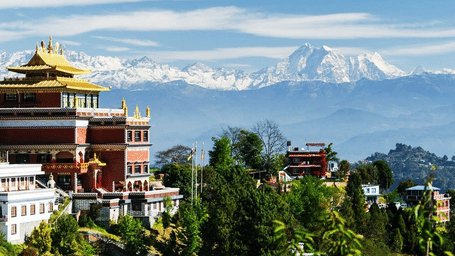 Golden-roofed Tibetan Buddhist monastery overlooking lush green hills and snow-capped Himalayan peaks in Kathmandu, Nepal.