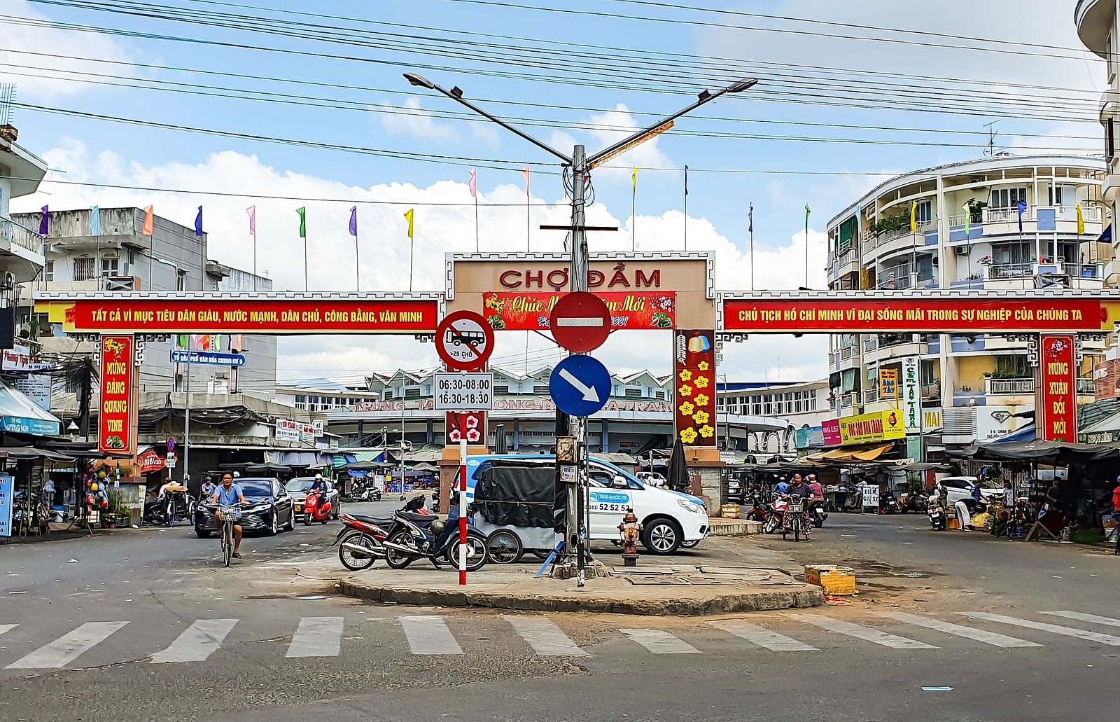 Street scene with a market entrance gate, signs, and traffic in an urban setting.