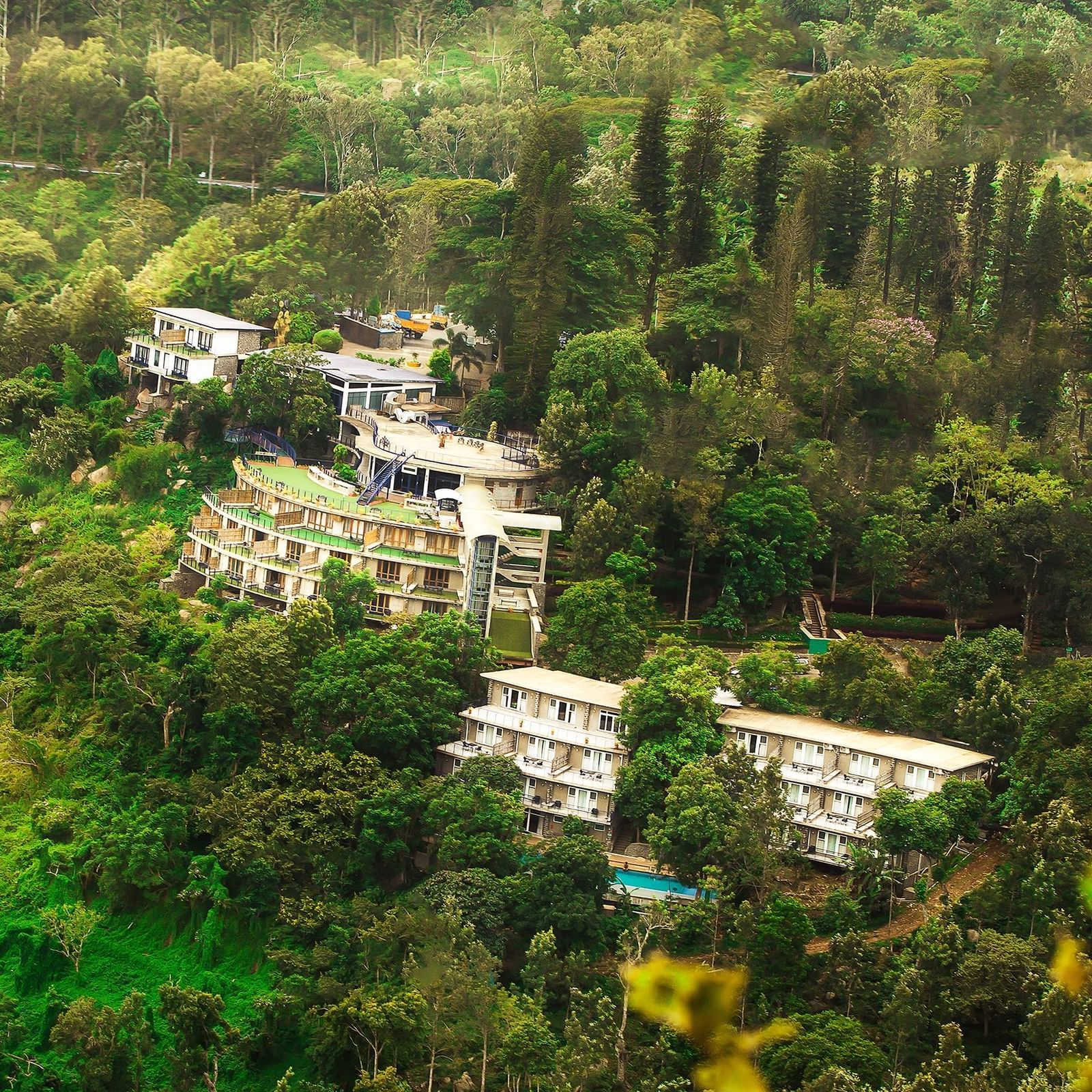 Drone shot of the hotel surrounded by mountains with sun light hitting the lush greenery - Great Trails Yercaud by GRT Hotels