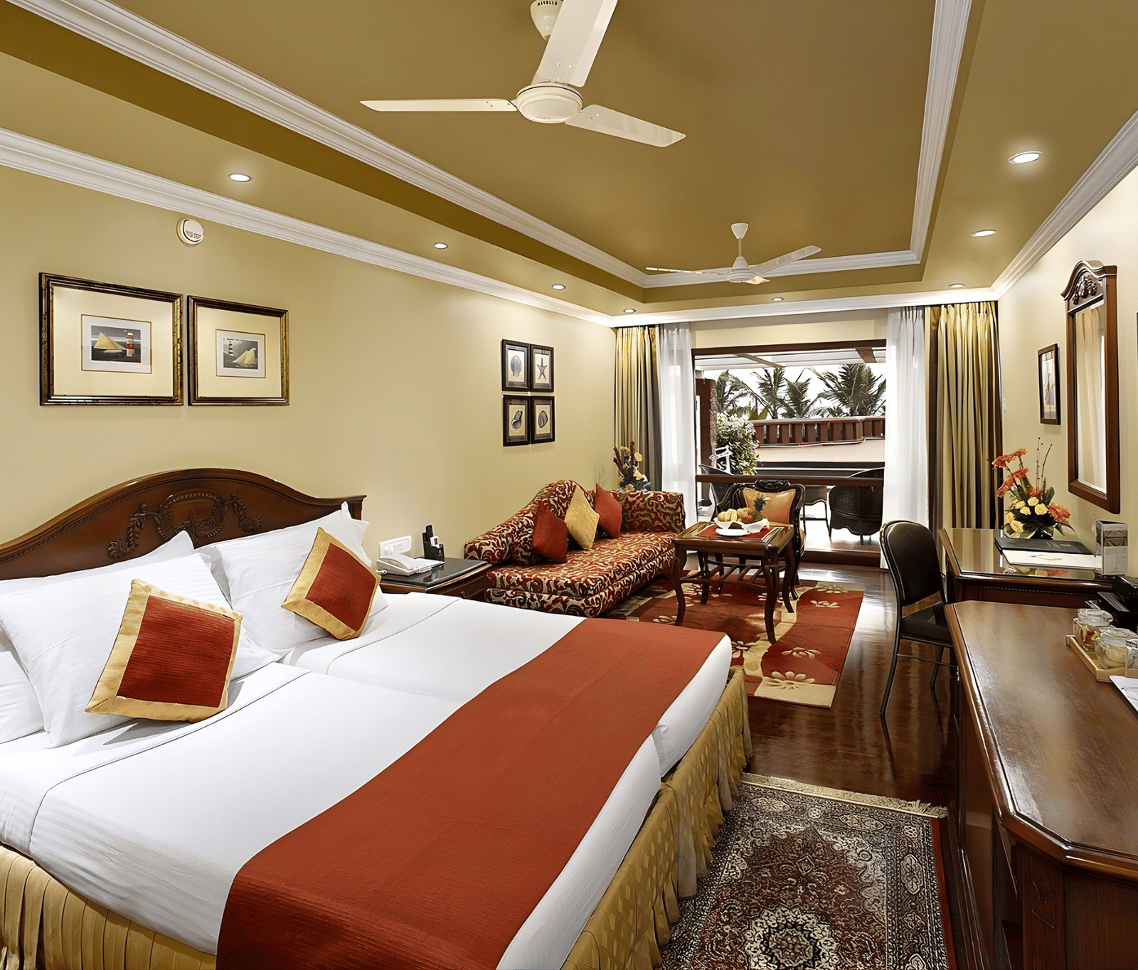 Spacious luxury suite with large double bed, red accents, comfortable sofa, and classic Indian decor at MAYFAIR Heritage Puri resort.