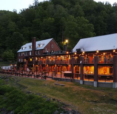 side view of our resort with bright yellow lighting with lush green pine forest in the background - Historic Tapoco Lodge