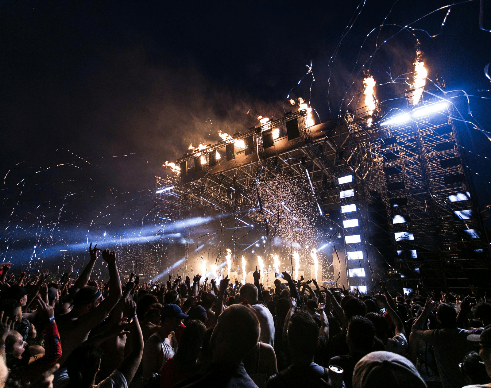 Enthusiastic audience enjoying a live music performance with flames and spotlights on stage.