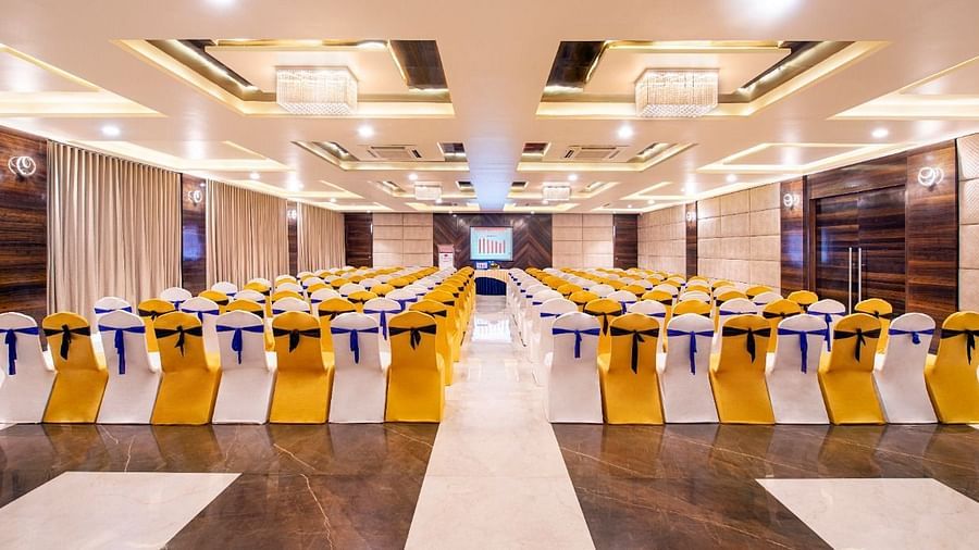 A well-lit event space at Lords Inn Porbandar, features round tables and chairs with yellow and blue accents.