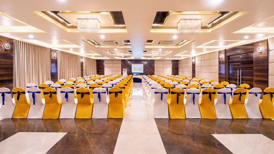 A well-lit event space at Lords Inn Porbandar, features round tables and chairs with yellow and blue accents.