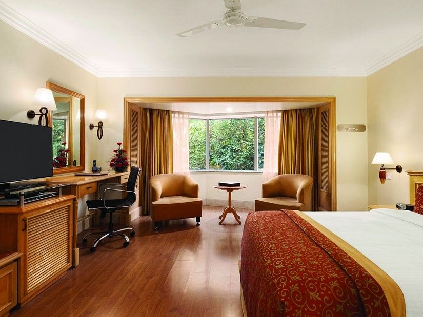 An image of a Deluxe Room featuring bed, flat screen TV, lamps, work desk, chair, sofa set and table - Ramada Plaza by Wyndham Palm Grove