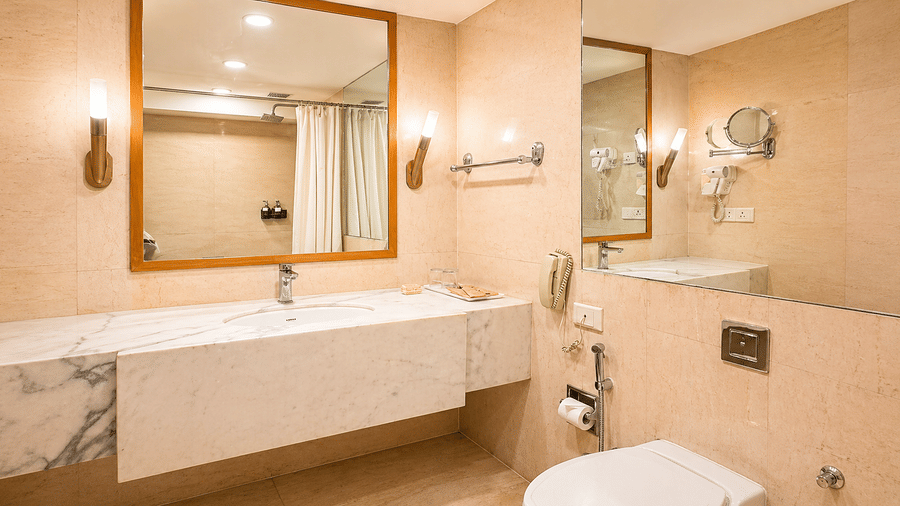 Bathroom with bathtub, wide mirror, sink, and beige-toned interiors at Pride Plaza Ahmedabad.
