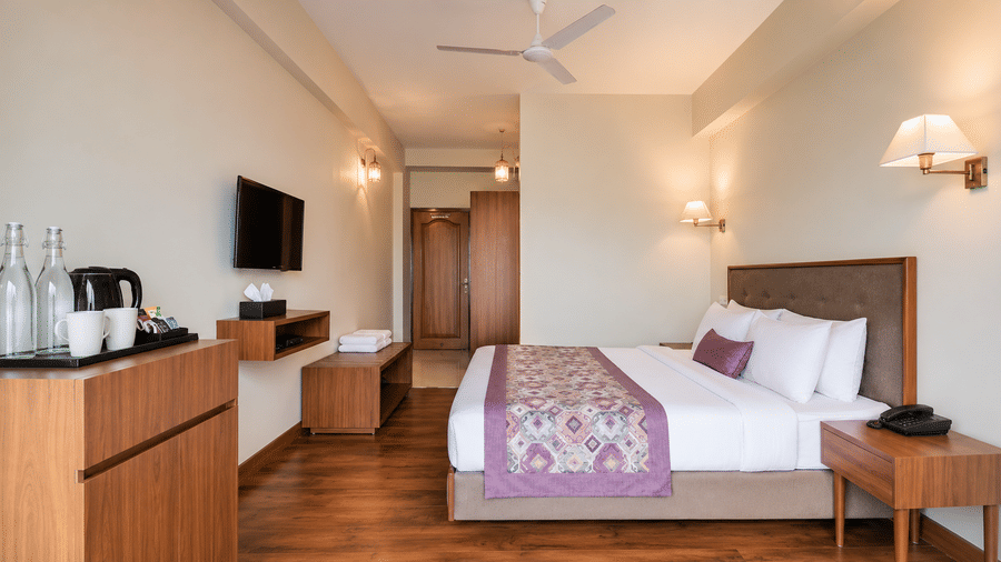 Guest room at Valmere Himalayan Hotel & Spa, Gangtok with a king-size bed, wooden flooring, a wall-mounted TV, and a dresser with a kettle and water bottles.