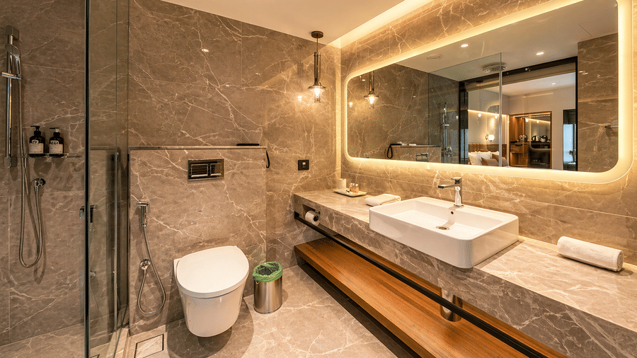 Spacious bathroom at Pride Premier Pune with twin wash basins, glass shower area and illuminated mirror.