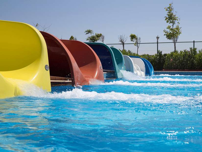 A row of multi-coloured water slides emptying into a bright blue swimming pool at a water park.