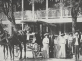 A vintage black and white photo shows the historic Tallman Hotel, with classic cars and people gathered outside its entrance.
