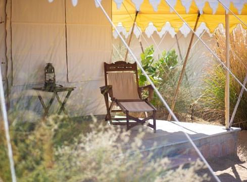 An image of the outdoor seating area of the tent with a chair and table and little vegetation - MANVAR Resort & Desert Camp