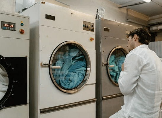 A person in a white shirt stands in front of several large washing machines with circular windows showing clothes inside.