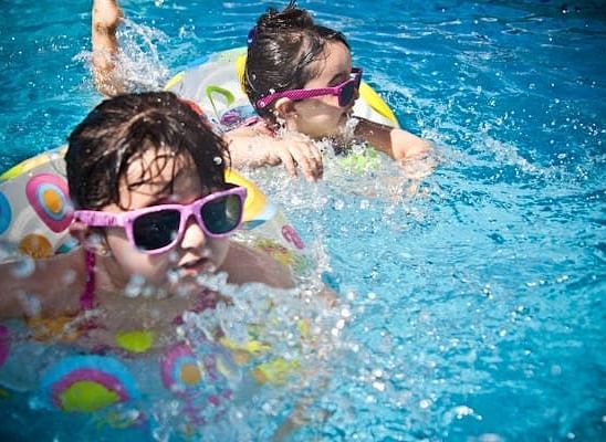 Two kids playing in a swimming pool with swimming floats on them.