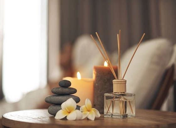 Relaxing spa-like scene with candles, diffuser, stones, and flowers.