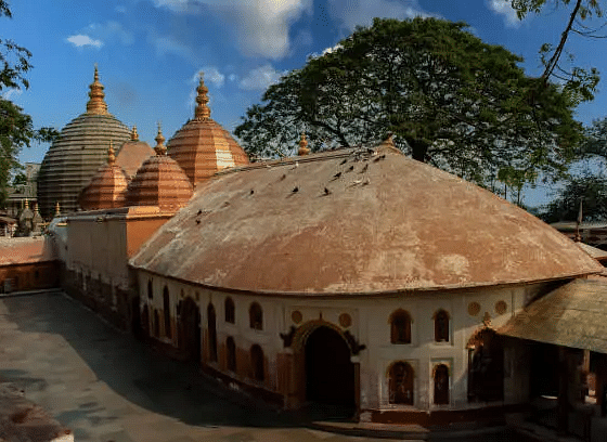 A temple complex with multiple domed structures, nestled among trees under a bright sky.