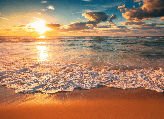 A beach view at sunrise with its reflection on the water, while clouds gather on the other side.