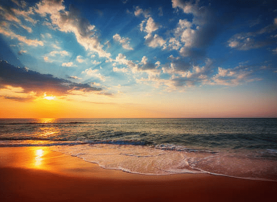 A sunset view from the beach shore with a cloudy sky.