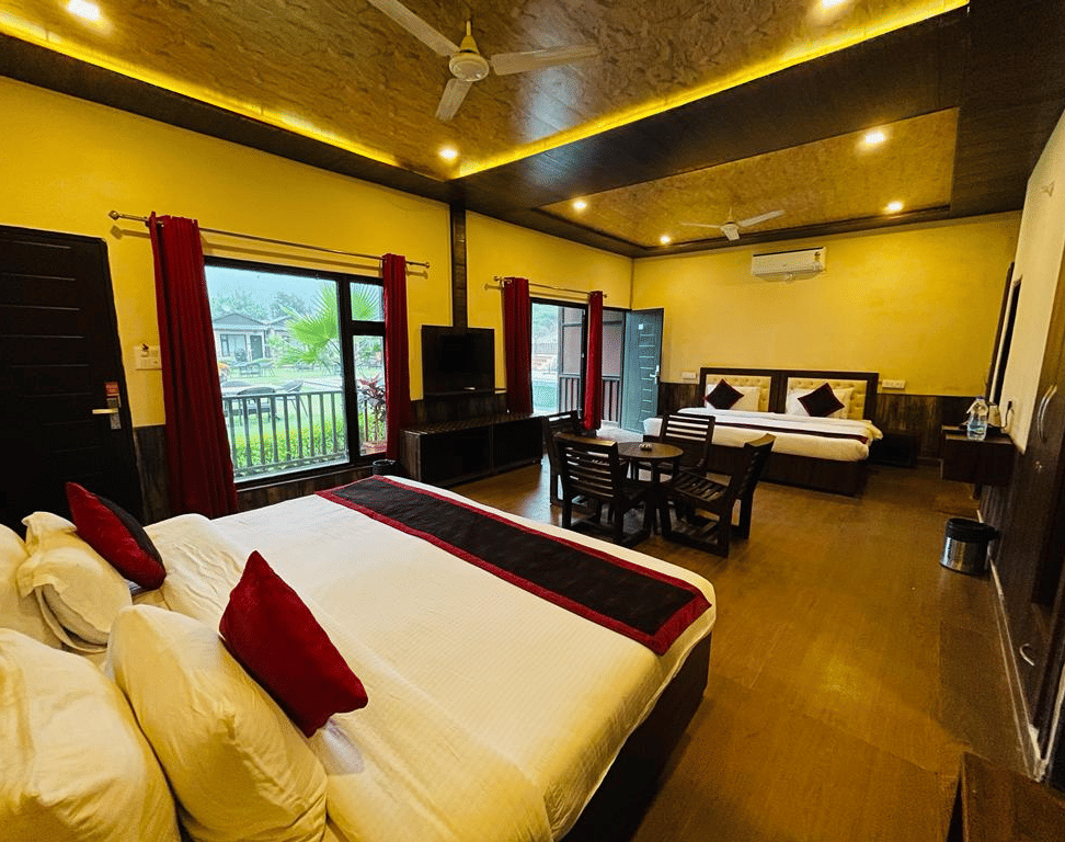 A Family Cottage with beds facing towards each other seperated by a round dining table and TV at DLS MJ River Resort, Rishikesh.