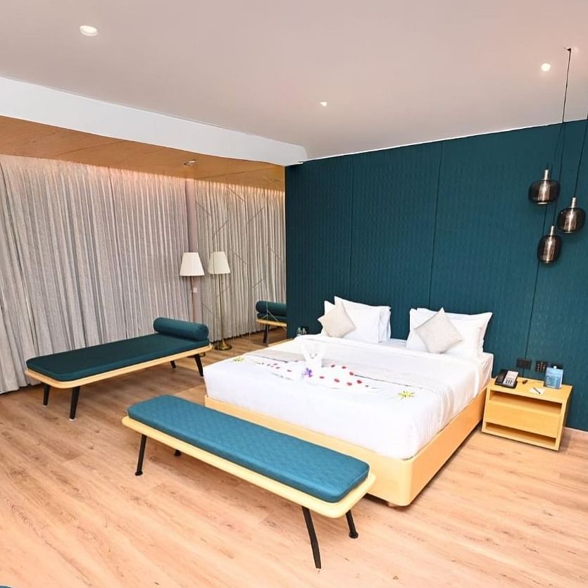 A bedroom in Dhanalakshmi Srinivasan Hotels, Perambalur, with a large bed, two lounge chairs, and two armchairs. The room features wooden flooring and a dark blue accent wall.