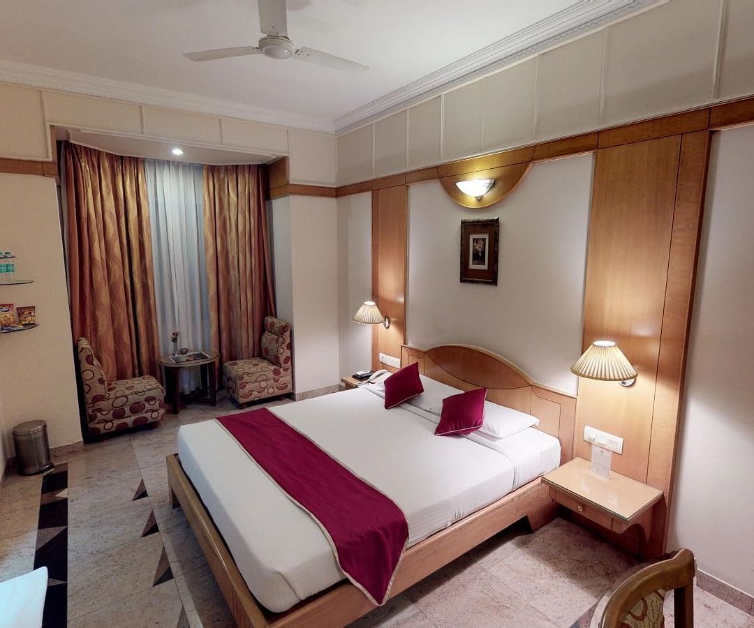 End to end view of the superior room at Hotel Pai Viceroy Jayanagar featuring a queen size bed, a television and a seating area with coffee table amongst other amenities