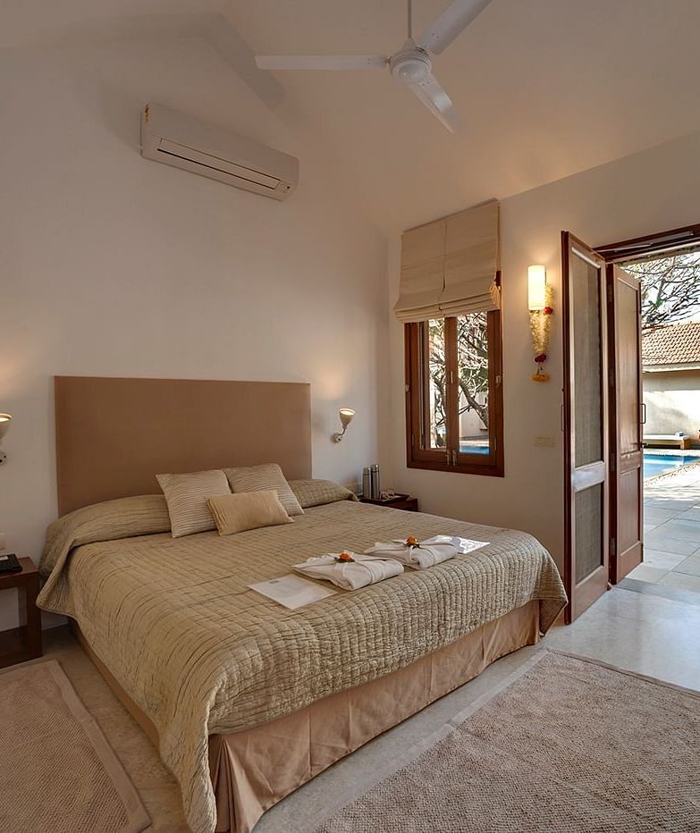 Neatly arranged bed with cushions and a view of the pool outside - Shreyas Retreat