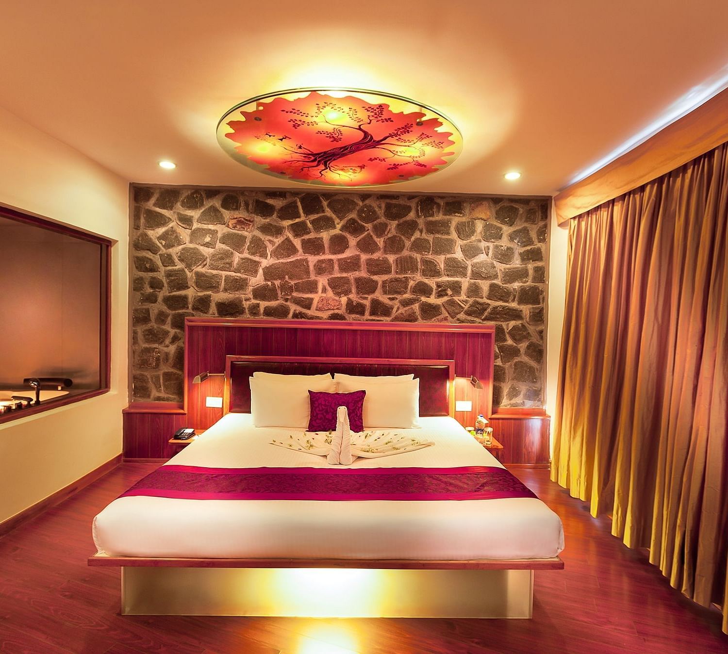 An image of a pent house with king size bed, sofa set, centre table, well lit room and expansive window with curtains - Great Trails Yercaud by GRT Hotels
