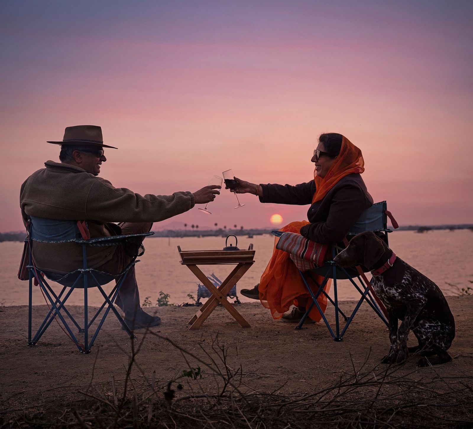 image of a couple enjoying the sunset as they cling wine glasses at Dev Shree, Deogarh
