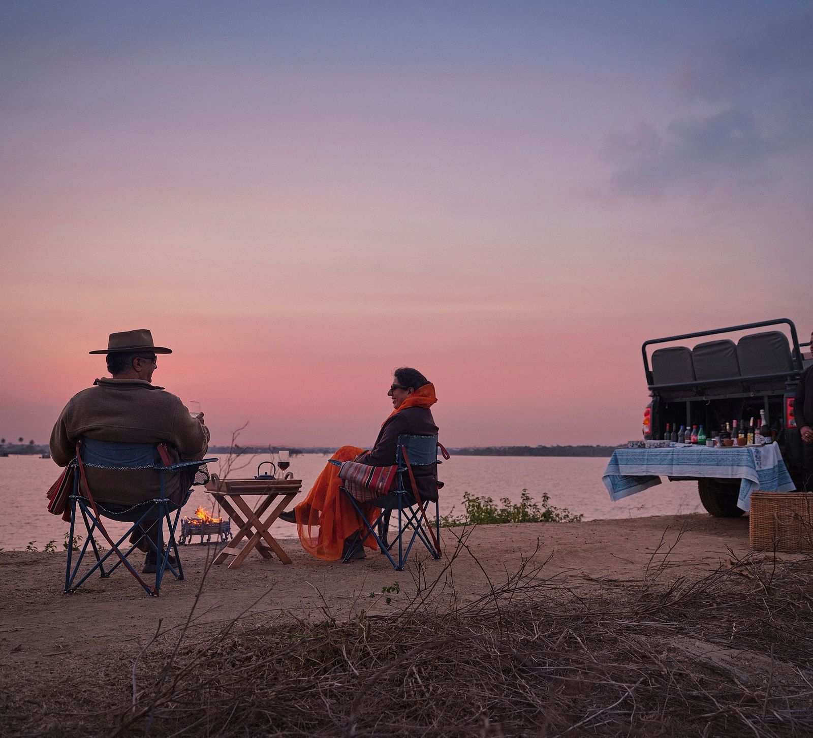couple soaking in the pink hues of the sunset with a picturesque lake in front of them at dev shree , deogarh