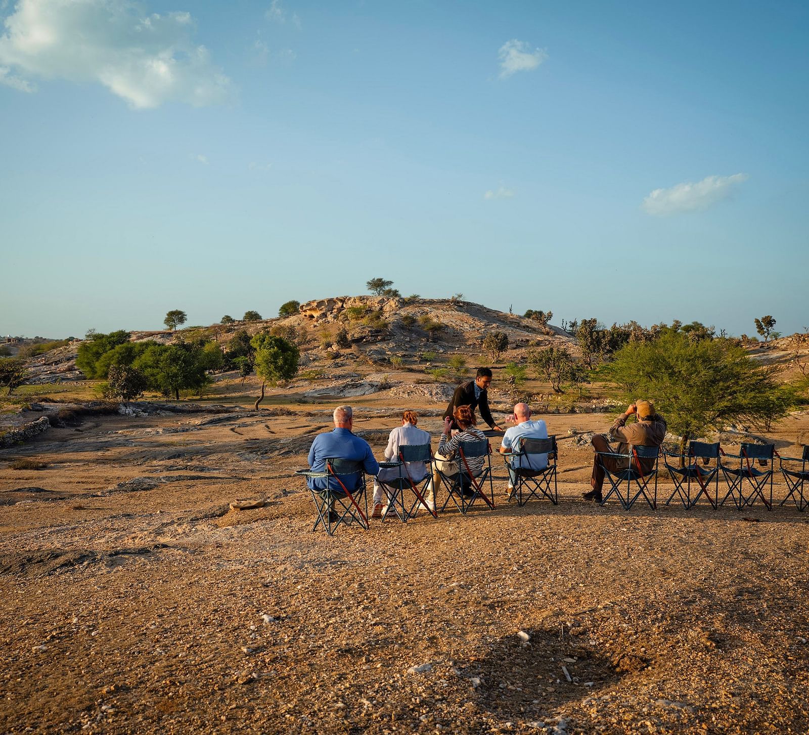 image of a few people sitting on chairs lined up in a rocky desert like area with very less green cover