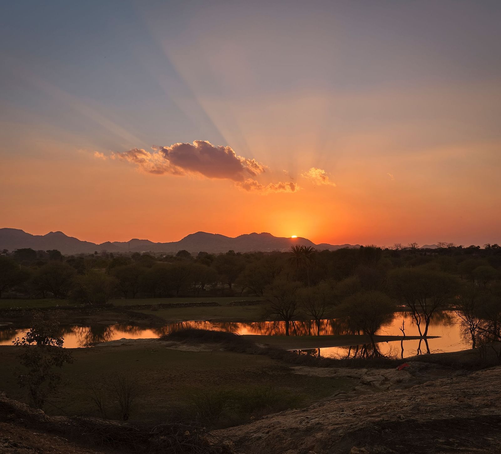 image of a beautiful sunset behind the aravalli range with a lake in the foreground witht he reflecction of the sunset