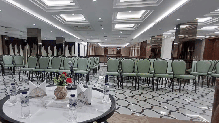 A wide view of a conference hall with rows of green chairs facing a central round table on a decorative tiled floor | Lawrence Solitaire Resort, Nainital