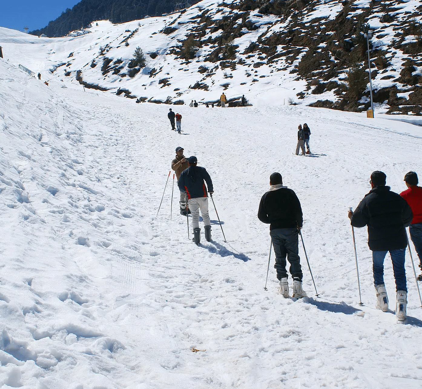 A group of people skiing down a snowy slope on a sunny day.