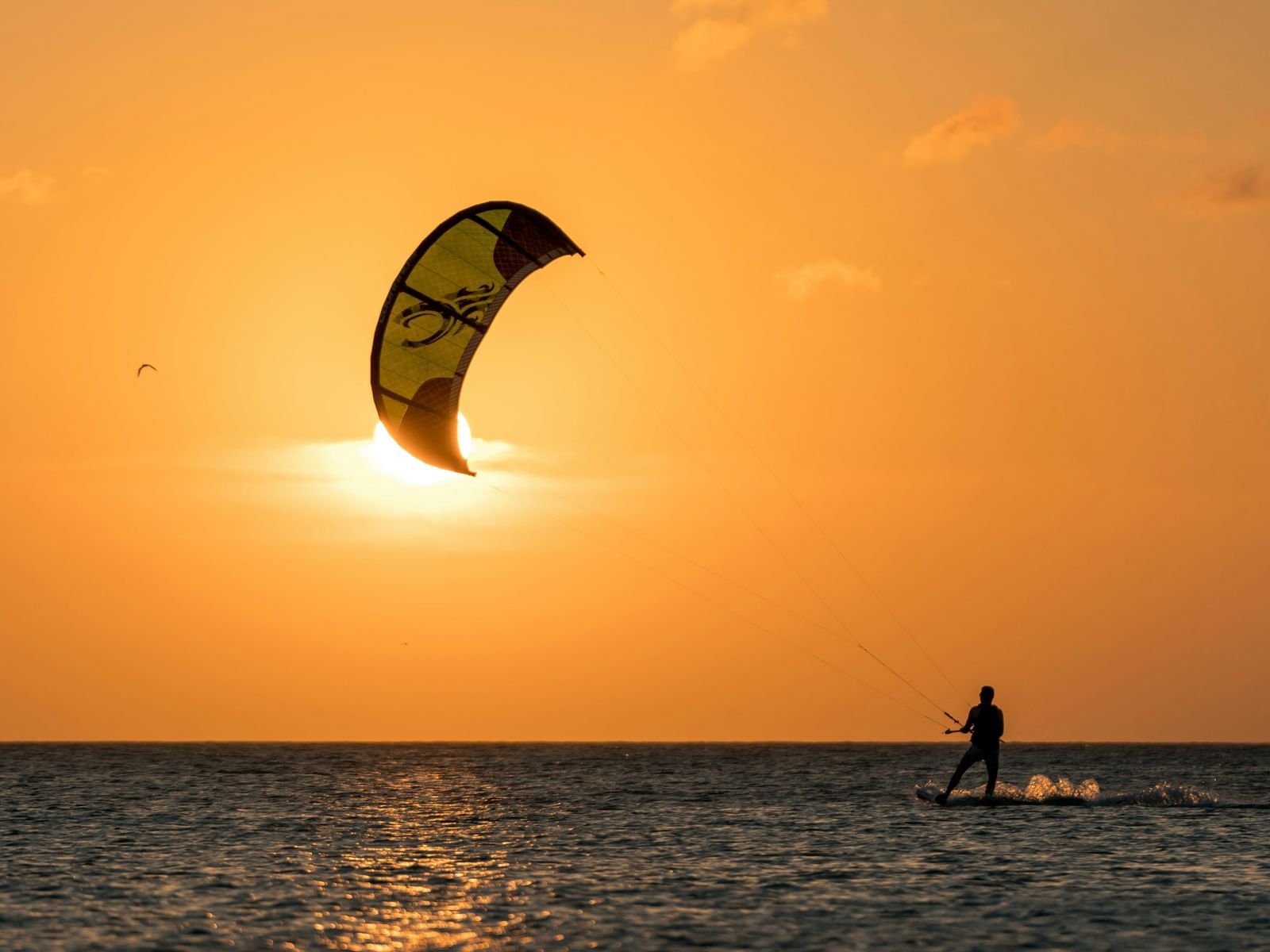 An overview of a person kite surfing on a beach with the setting sun in the background - one of the best Mui Ne Beach Activities