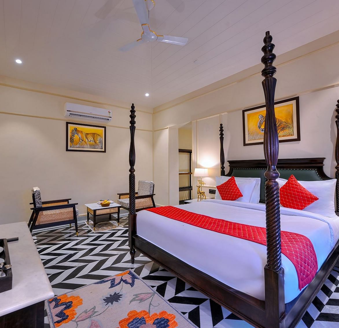 Premium Suite Cottage with a dark wood four-poster bed featuring red accents, black and white chevron flooring, a seating area with two chairs, air conditioning, and framed artwork - Singhvilas, Ranthambore